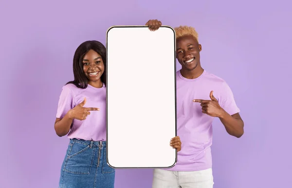 Excited black couple showing white empty smartphone screen — Stock Photo, Image