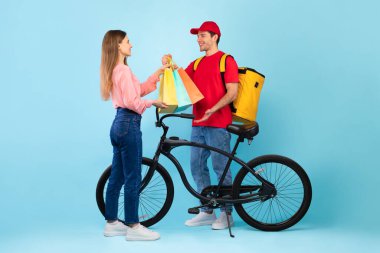 Bisikletli Kurye, mavi arka plandaki bayana alışveriş çantası veriyor.