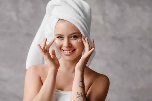 Koncepcja pielęgnacji ciała. Portret pięknej młodej damy z kremem na policzkach i białym ręcznikiem na głowie uśmiechniętym do kamery — Zdjęcie stockowe