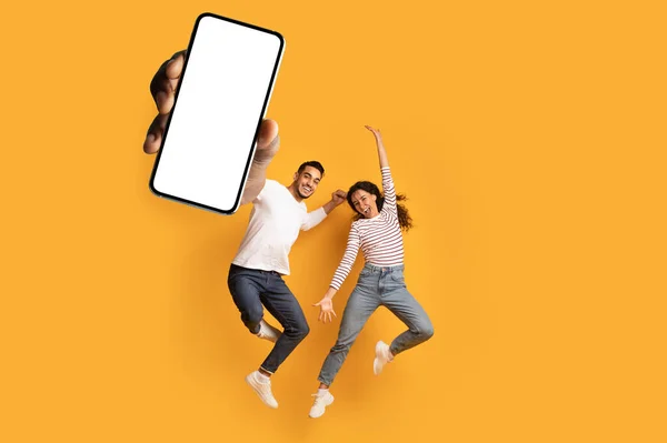 Vaya, buenas noticias. Pareja llena de alegría mostrando un enorme smartphone con pantalla blanca en blanco, saltando y celebrando la victoria — Foto de Stock