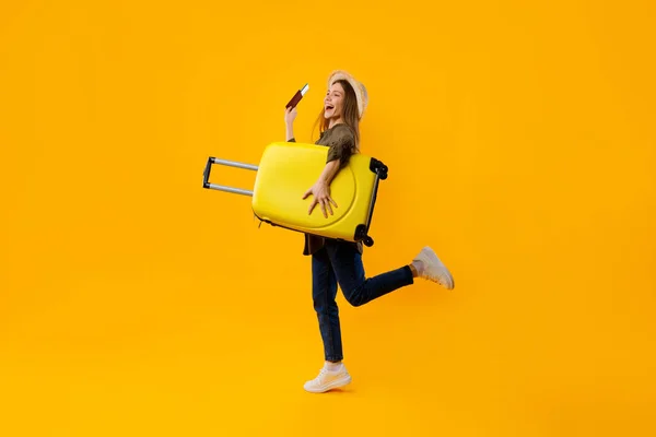 Alegre feminino turista segurando mala e passaporte sobre fundo amarelo — Fotografia de Stock