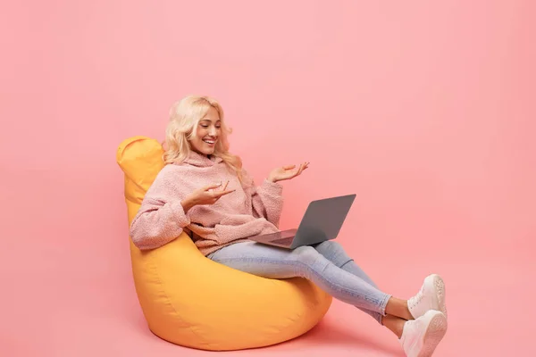 Ευτυχισμένη γυναίκα κάνει βιντεοκλήση στο laptop, ενώ κάθεται σε καρέκλα beanbag, συναισθηματικά μιλώντας στην οθόνη του υπολογιστή — Φωτογραφία Αρχείου