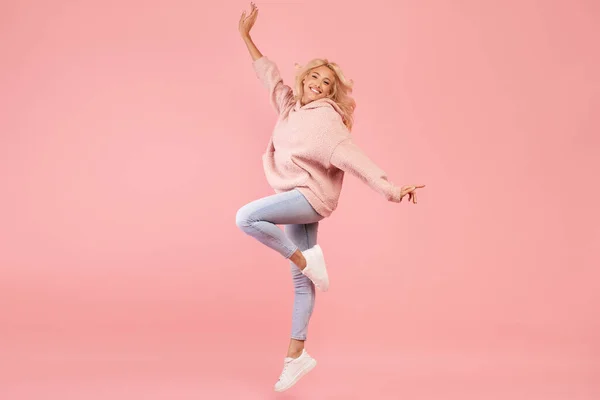 Игривая белая женщина прыгает и веселится на розовом фоне студии, женщина позирует в воздухе — стоковое фото