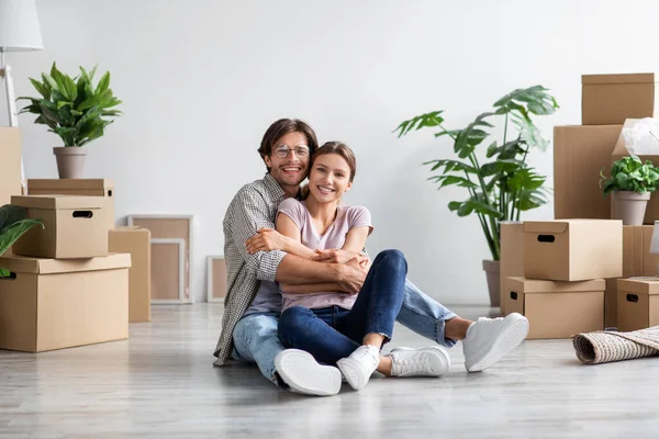 Satisfied european young guy in glasses in casual hugging female, sit on floor with cardboard boxes — Stock Photo, Image