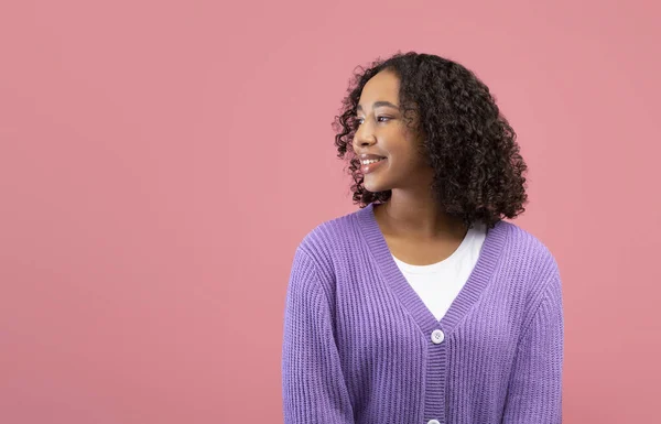 Bastante joven dama negra en ropa casual sonriendo y mirando a un lado en el espacio en blanco sobre fondo de estudio rosa — Foto de Stock