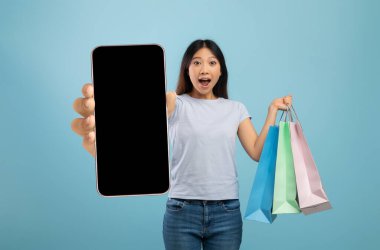 Alışveriş torbaları ve boş ekranlı akıllı telefon tutan duygusal kadın.