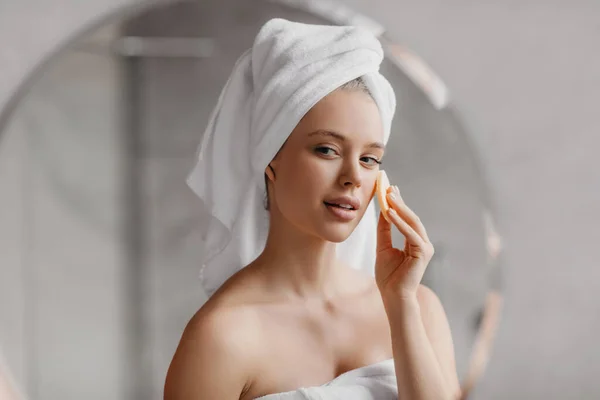 Όμορφη κυρία που χρησιμοποιεί διακοσμητικό σφουγγάρι απολαμβάνοντας τη ρουτίνα περιποίησης προσώπου, στέκεται στο μπάνιο το πρωί — Φωτογραφία Αρχείου
