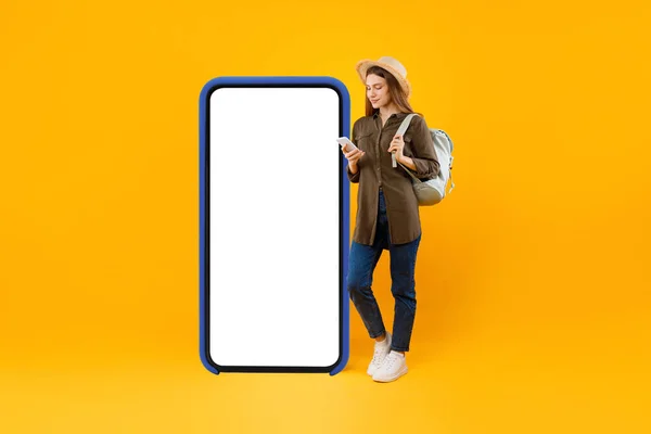 Turystka korzystająca ze smartfona przy dużym ekranie telefonu, żółte tło — Zdjęcie stockowe