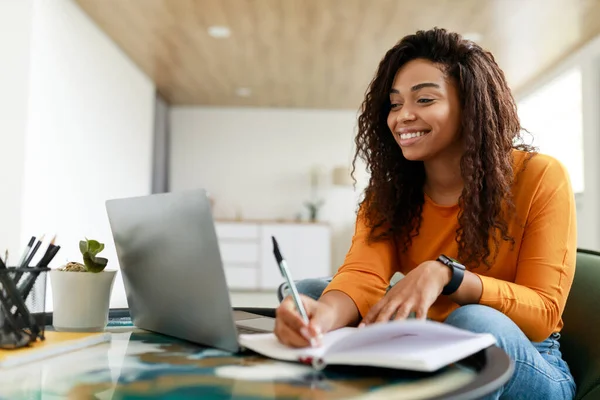 Mulher negra sentada na mesa, usando a escrita do computador no caderno — Fotografia de Stock