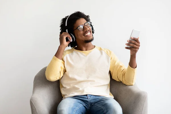 Онлайн-стриминговые сервисы. Веселый черный парень сидит на волосах и слушает музыку — стоковое фото