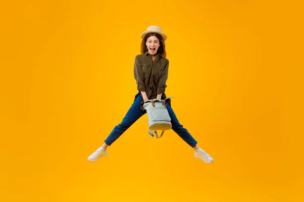 Excited Woman Holding Backpack Jumping In Mid Air, Yellow Background — Stock Photo, Image