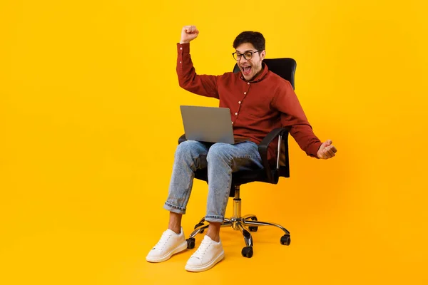 Uomo gioioso guardando il computer portatile che trema pugni, sfondo giallo — Foto Stock