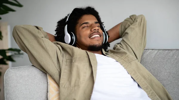 Agradado afro-americano cara ouvir música em fones de ouvido sem fio em casa — Fotografia de Stock