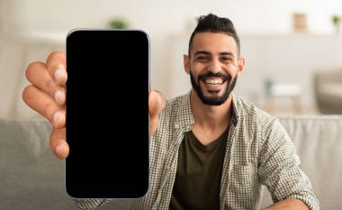 Boş ekranlı cep telefonu gösteren mutlu bir Arap.