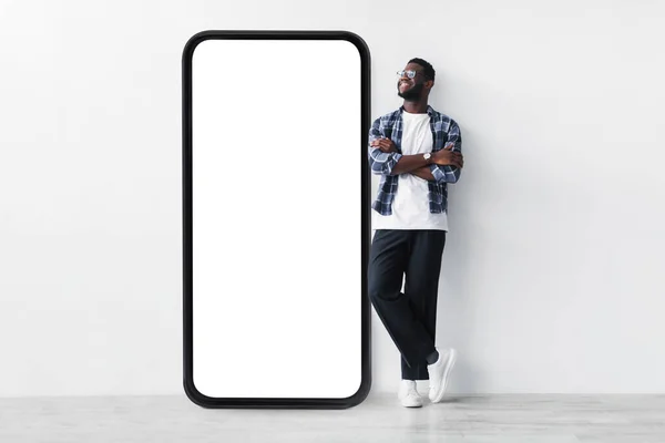 全身上下都是黑人，站在巨大的智能手机旁边，带着空白的白屏模板，模仿着 — 图库照片