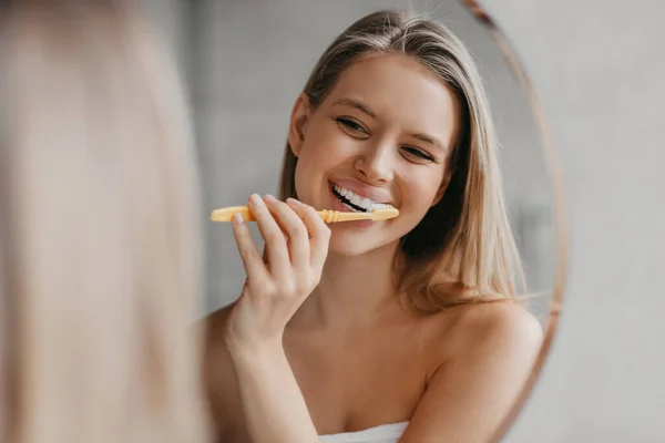 Higiene bucal, dientes sanos y cuidado. Mujer joven cepillándose los dientes con cepillo de dientes y mirándose en el espejo en el baño —  Fotos de Stock