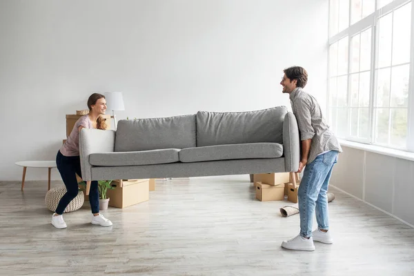 Glad europeisk ung man och kvinna bära soffa i tomt rum med pappkartonger — Stockfoto