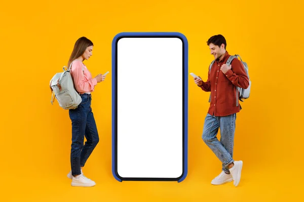 Coppia di turisti che utilizzano telefoni cellulari vicino a grande smartphone, sfondo giallo — Foto Stock