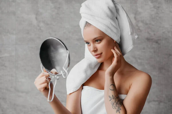 Conceito de tratamento facial. Bela senhora caucasiana em toalha na cabeça segurando espelho e tocando sua pele macia perfeita — Fotografia de Stock