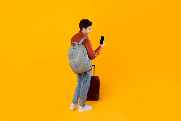 Turista cara usando Smartphone em pé com bagagem sobre fundo amarelo — Fotografia de Stock