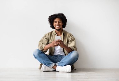 Çevrimiçi İletişim. Yerde dinlenirken akıllı telefondan mesaj atan mutlu siyah adam.