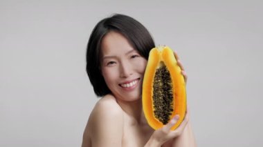 Orta yaşlı Koreli Kadın Papaya 'yı Yüze Yakın Tutuyor, Gri Arkaplan