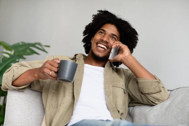 Mutlu Afrikalı Amerikalı adam cep telefonuyla konuşuyor ve evde kahve içiyor.