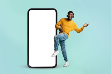 Güzel müzik uygulaması. Büyük bir akıllı telefonun yanında boş ekranla dans eden heyecanlı siyah adam kulaklıkla müzik dinliyor.
