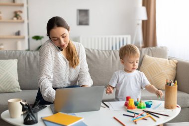Bebekle çalışıyorum. Küçük oğlu yakınlarda oynarken, genç bir anne cep telefonuyla konuşuyor ve dizüstü bilgisayarda yazıyor.