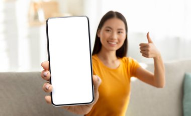 Neşeli genç Asyalı kadın boş ekranlı akıllı telefon gösteriyor.