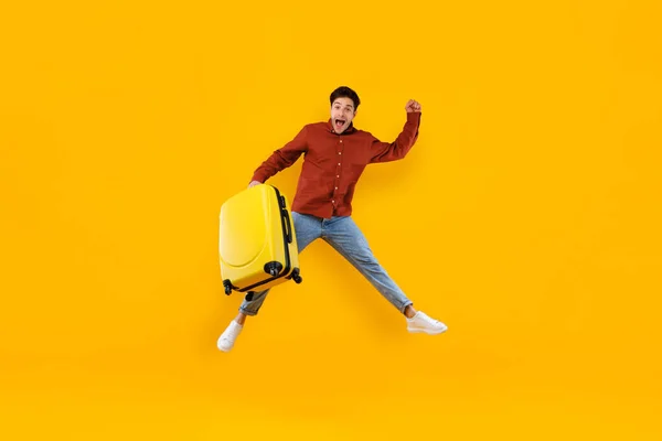 Masculino viajante salto segurando grande mala sobre fundo amarelo — Fotografia de Stock