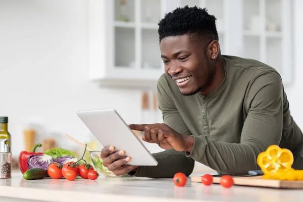 Online Recipe. Smiling Black Guy Using Digital Tablet In Kitchen While Cooking — Stock Photo, Image