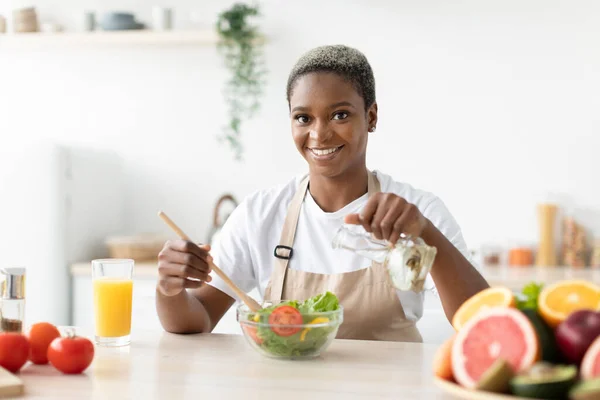 Sorridente donna millenaria afroamericana in grembiule fare insalata a tavola — Foto Stock