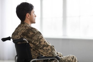 Tekerlekli sandalyede oturup pencereden bakan düşünceli asker.