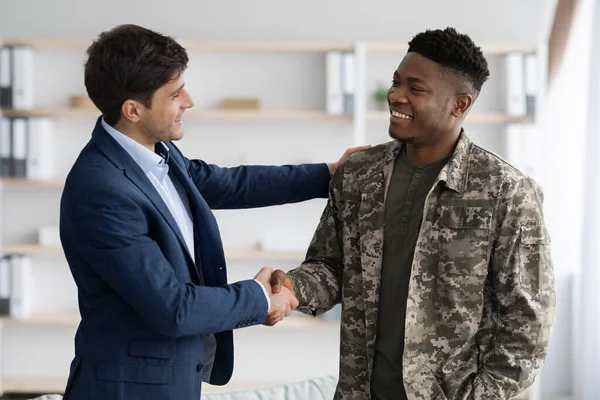Cheerful guy in suit shaking black military man hand — Stock Photo, Image