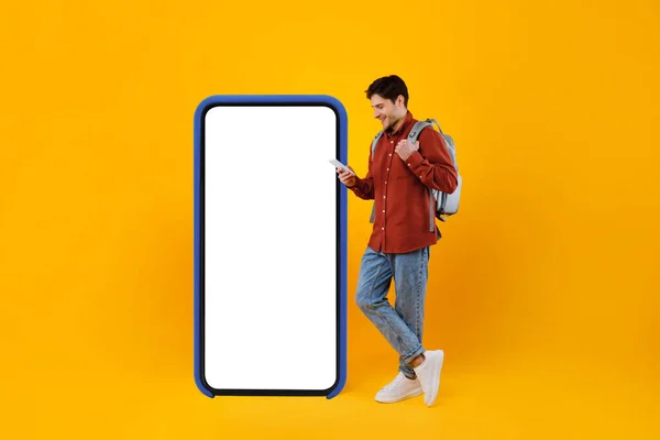 Reiziger die telefoon gebruikt die in de buurt van een grote mobiele telefoon staat, gele achtergrond — Stockfoto
