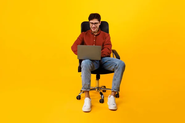 Uomo che utilizza computer portatile seduto in sedia su sfondo giallo — Foto Stock