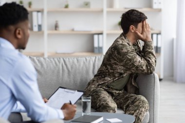 Kamuflajlı üzgün adam psikologla konuşurken ağlıyor.