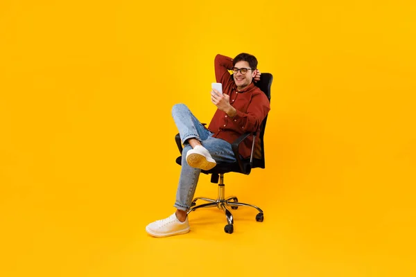 Hombre usando Smartphone sentado en la silla mensajes de texto sobre fondo amarillo — Foto de Stock