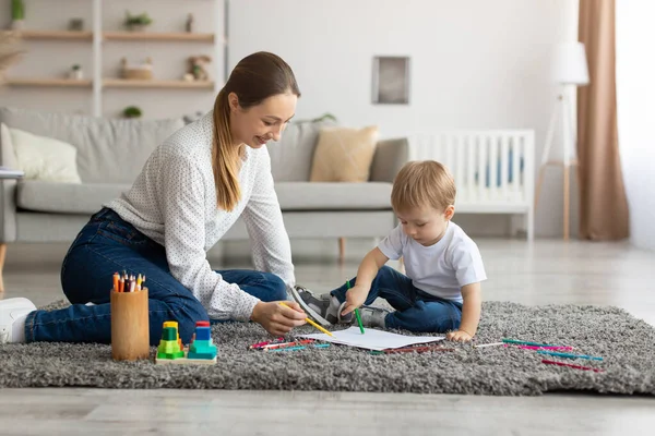 Ελεύθερος χρόνος με το μωρό. Ευτυχισμένη μητέρα και παιδί γιο σχέδιο με πολύχρωμα μολύβια, χαλαρώνοντας μαζί στο πάτωμα στο σαλόνι — Φωτογραφία Αρχείου