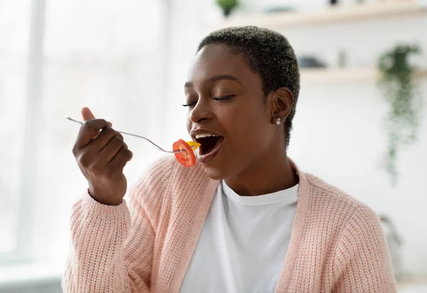 Mujer negra joven satisfecha en casual con los ojos cerrados disfrutar de deliciosa ensalada orgánica, comer trozo de verdura —  Fotos de Stock