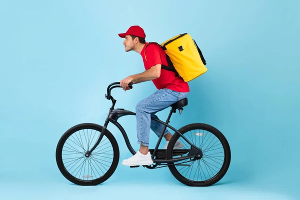 Koerier Guy Riding Bike leveren maaltijd, blauwe achtergrond, zijaanzicht — Stockfoto