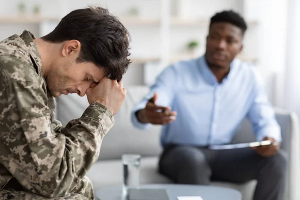 Distressed young man soldier attending therapy session with psychiatrist