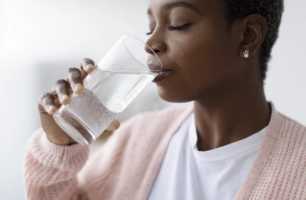 Millennial african american lady in casual drink water from glass in kitchen interior, profile, close up