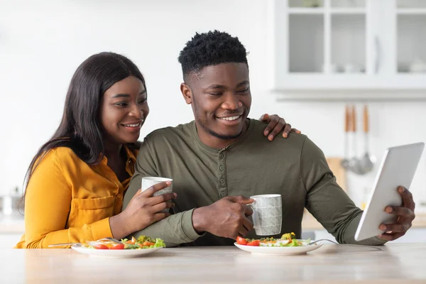 Joven pareja negra desayunando juntos y usando tableta digital en la cocina —  Fotos de Stock