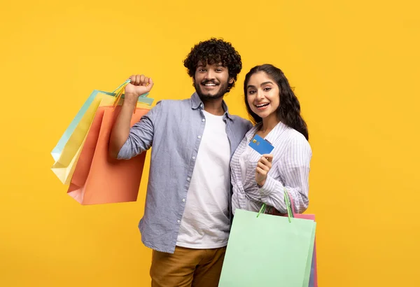 Pago fácil. Retrato de pareja india mostrando bolsas de comprador con tarjeta de crédito de débito después de compras en el centro comercial — Foto de Stock