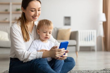 Çocuklar ve teknolojiler. Mutlu anne ve oğlu akıllı telefon kullanıyor, yeni uygulamalara bakıyor ya da internetten alışveriş yapıyor.