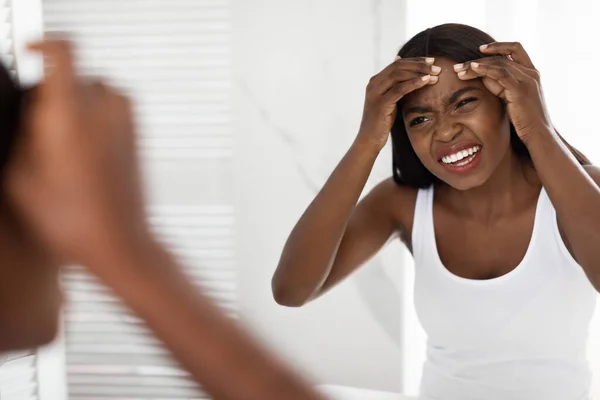 Mulher negra infeliz com problema pele Popping Pimple na testa perto do espelho — Fotografia de Stock