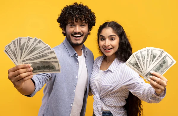 Gran suerte y concepto de ganar. Emocionada pareja india joven sosteniendo dinero en efectivo, posando con dinero sobre fondo amarillo — Foto de Stock