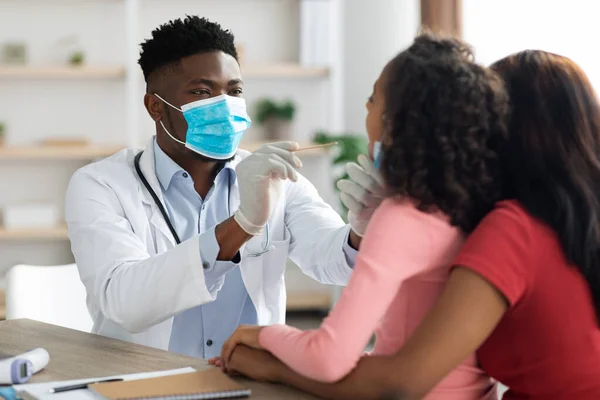 Médico negro revisando la garganta del niño, madre y salchicha en la clínica —  Fotos de Stock